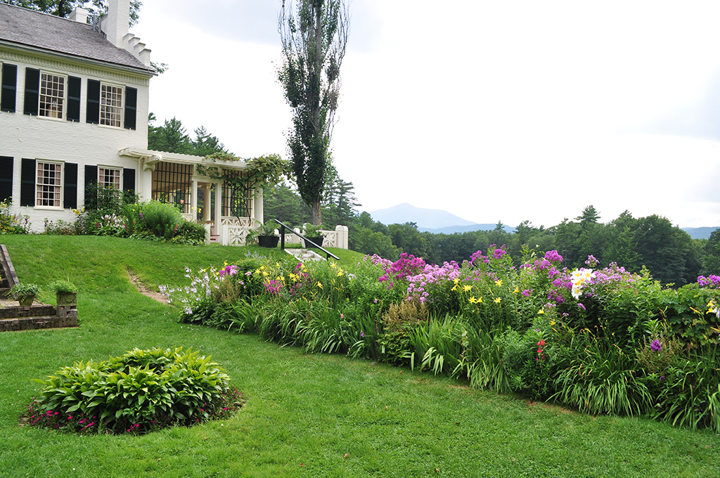 List of National Parks by State: A Complete List of All 400+ US National Parks 42 A white house with black shutters. There are small mountains in the background. In the front lawn, which is bright green, we see gardens of yellow, pink, red, white, and purple flowers.