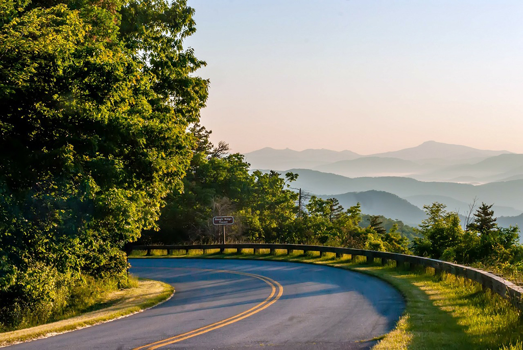 List of National Parks by State: A Complete List of All 400+ US National Parks 46 A paved road rounds a corner in the forest. We can see blue mountains in fog in the distance.