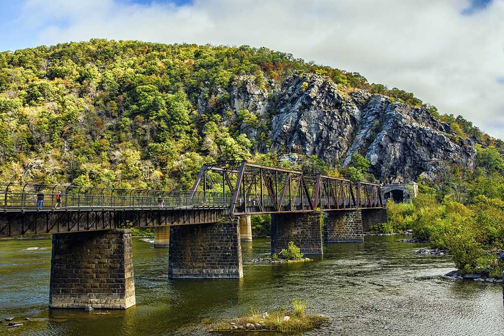 List of National Parks by State: A Complete List of All 400+ US National Parks 61 A metal bridge over a river toward a hill with a cliff rock face and green trees