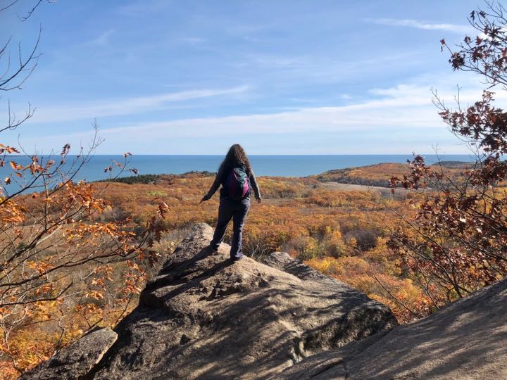 How to Hike the Heart-Stopping Precipice Trail in Acadia National Park 17 A woman stands on a rock outcropping overlooking fall foliage near a bay