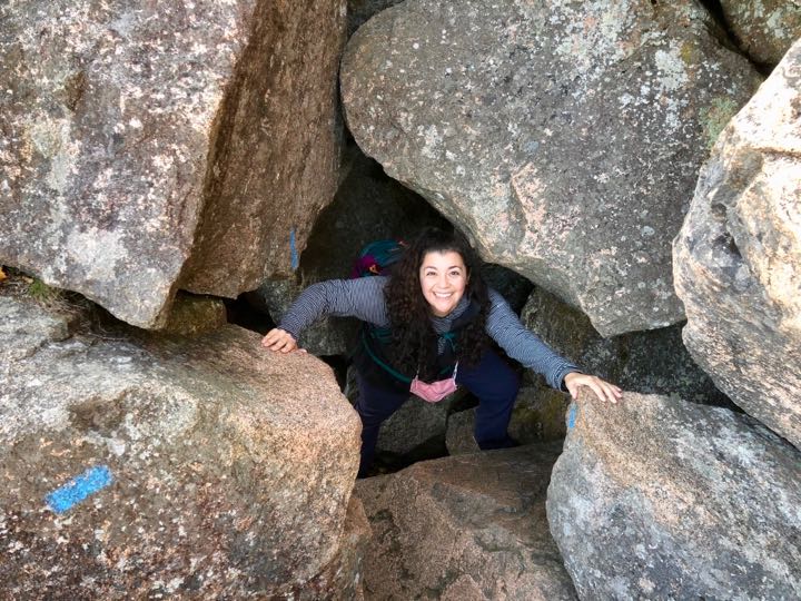 How to Hike the Heart-Stopping Precipice Trail in Acadia National Park 14 A woman smiles while climbing through a field of boulders