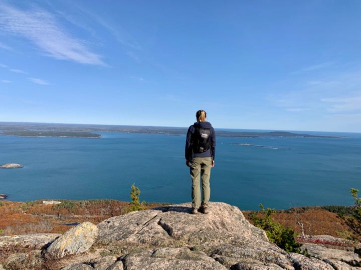 How to Hike the Heart-Stopping Precipice Trail in Acadia National Park 19 A woman stands on top of a mountain taking in the view over the bay