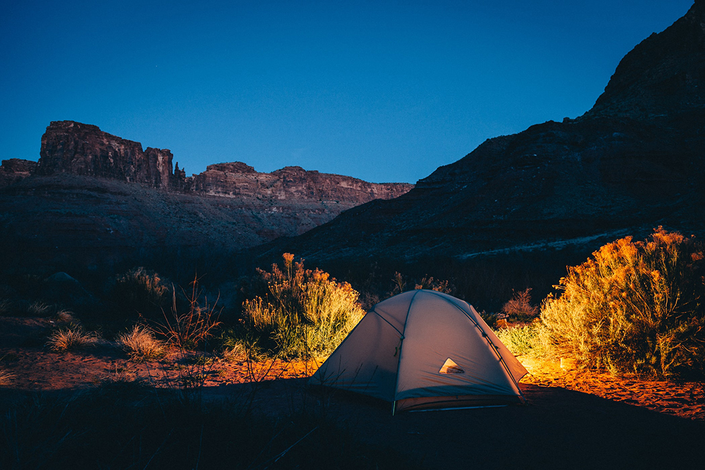 Visiting Canyonlands National Park: The Expert Travel Guide 9 A tent lit up at night below rocky mountains