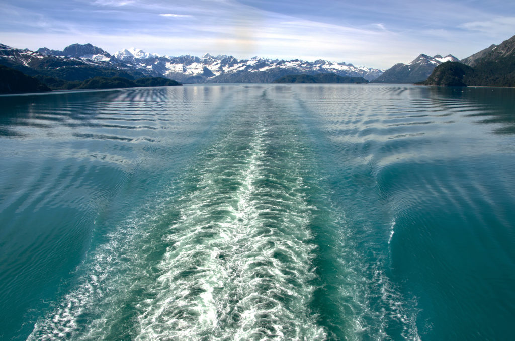 16 Astonishing National Parks in Alaska 11 Waves from a boat in water below mountains in Glacier Bay, one of the national parks in Alaska