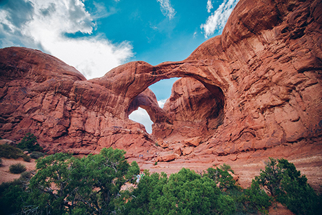 10 Best Hikes in Arches National Park That Lead to the Greatest Natural Arches in Utah 6 Green brush below two circular arches in red rock. Double Arch is one of the best hikes in Arches National Park