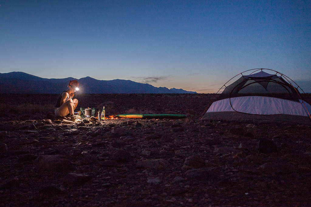 Camping in Death Valley National Park: The Ultimate Guide to All 9 Campgrounds in Death Valley 16 A woman with a lit headlamp sitting at a campsite next to her tent while camping in Death Valley National Park
