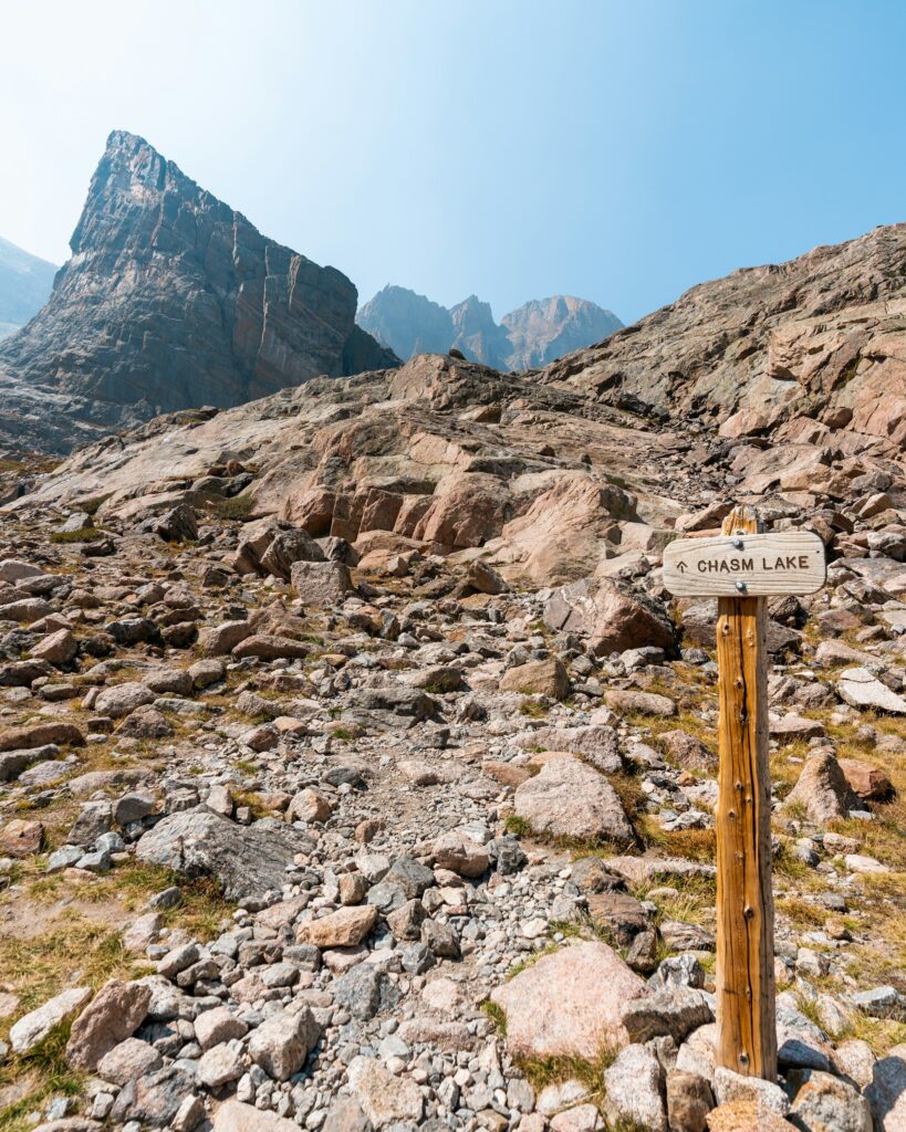 The 26 Best Hikes in Rocky Mountain National Park for Every Hiker 2 A wooden sign reads "Chasm Lake" along a rocky trail that leads to a jagged peak
