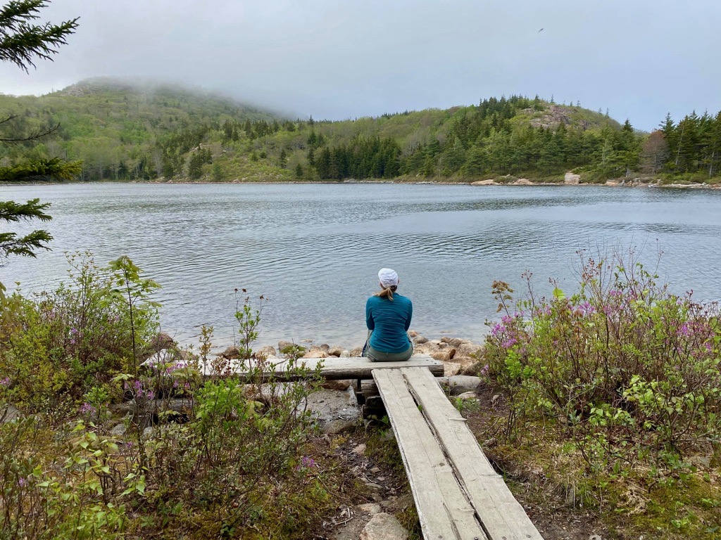 15 of the Best Hikes in Acadia National Park: Exploring Mount Desert Island 55 A hiker sits on a wooden boardwalk overlooking The Bowl, a small pond in Acadia National Park.