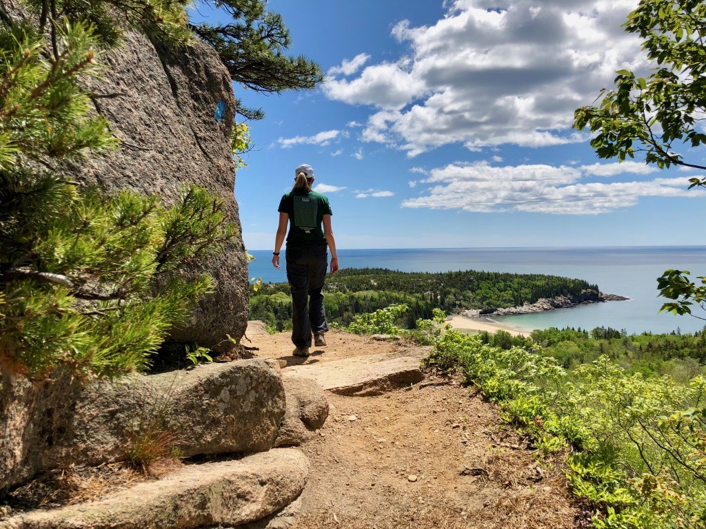 Un randonneur marche sur une corniche étroite à côté d'une falaise sur le Beehive Trail