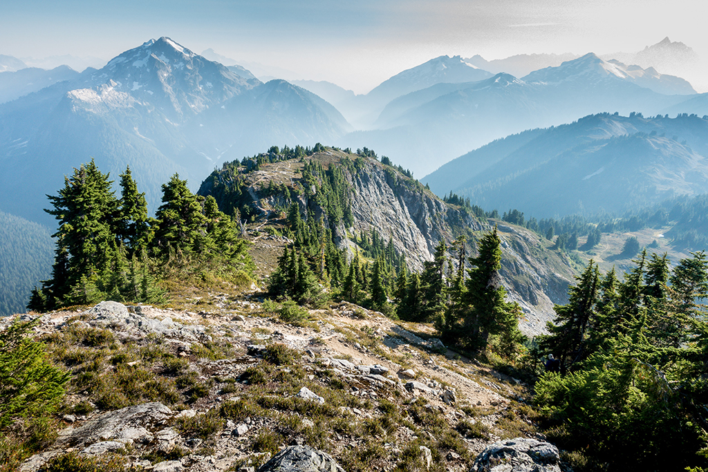List of US National Parks in Alphabetical Order (All 400+!) 31 A rocky dome with scattered green trees in the foreground with hazy blue mountains in the background