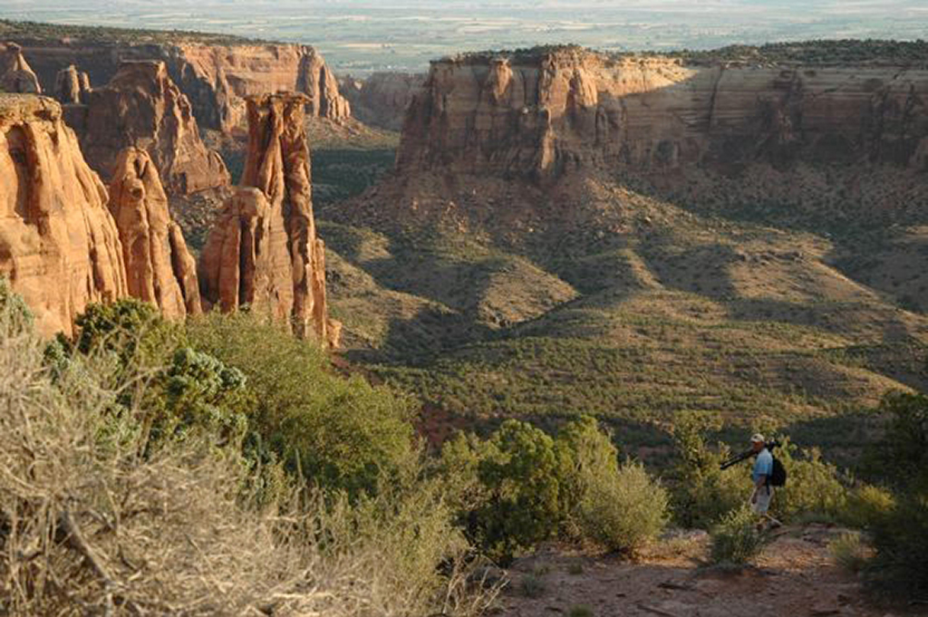 12 Breathtaking National Parks in Colorado 12 A hiker starts his trek into a rocky canyon with red monoliths. Colorado National Monument is one of the Colorado national parks.