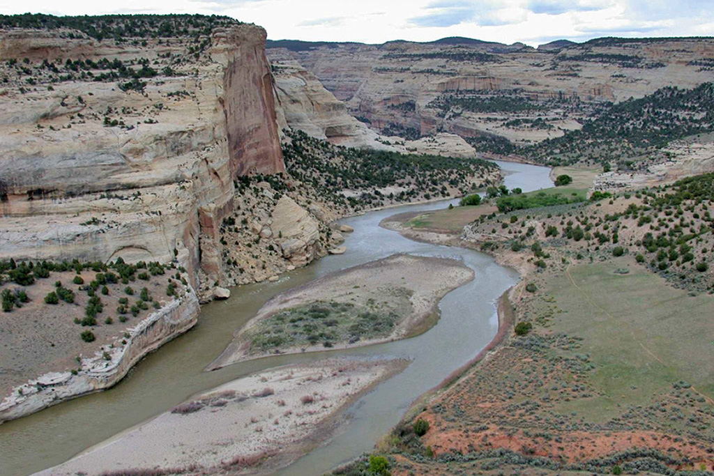 12 Breathtaking National Parks in Colorado 14 A river curves through a carved canyon among green grass and red rock. Dinosaur National Monument is one of the national parks in Colorado.