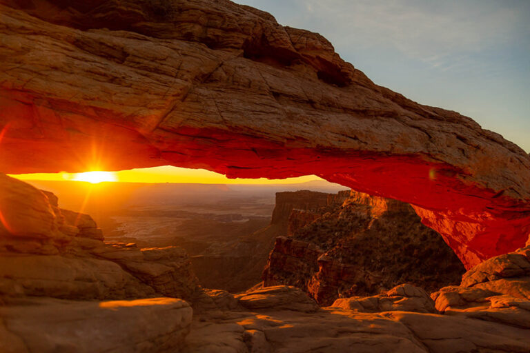 The sun rises over Canyonlands, one of the national parks in Utah. Here, it's seen cresting between the horizon and a rock arch.