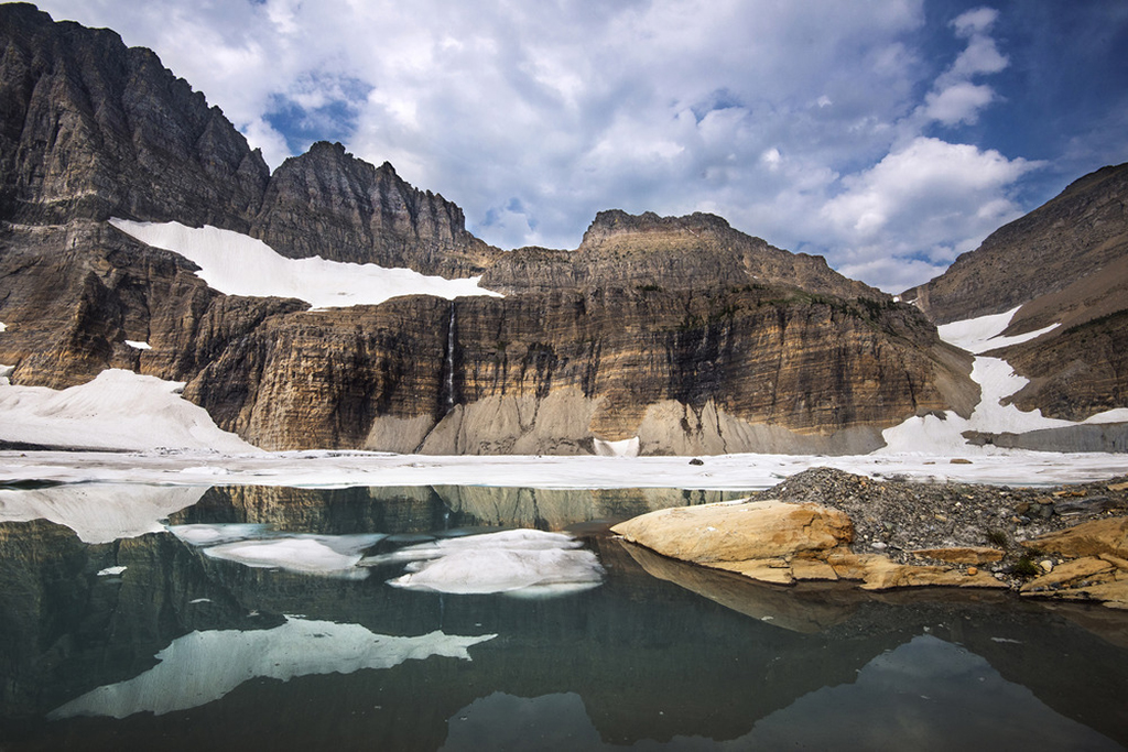 8 Marvelous National Parks in Montana 8 A glacier sits above a pool of water on a brown mountain