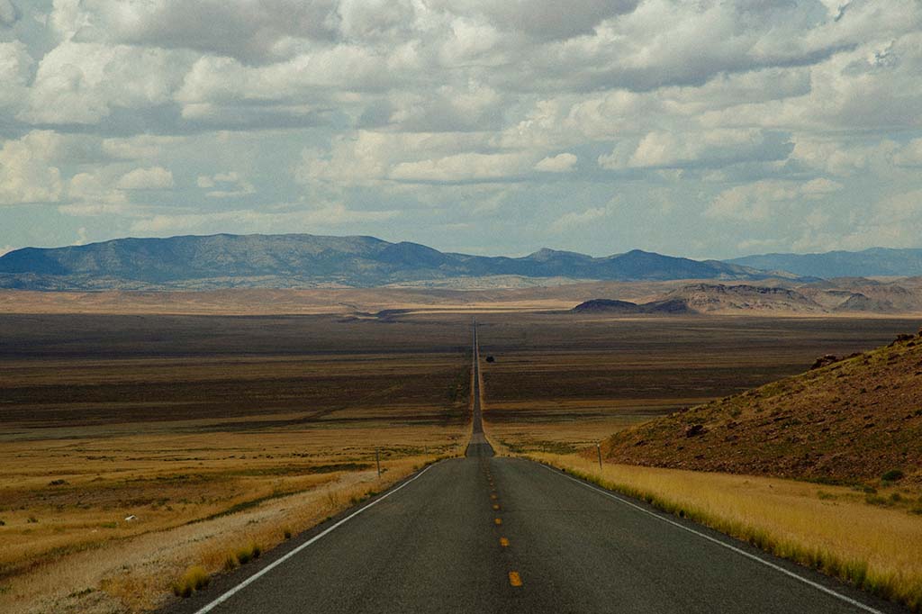 A paved road surrounded by a vast prairie leading to a mountain range. Great Basin, one of the national parks in Nevada, is in the distance.
