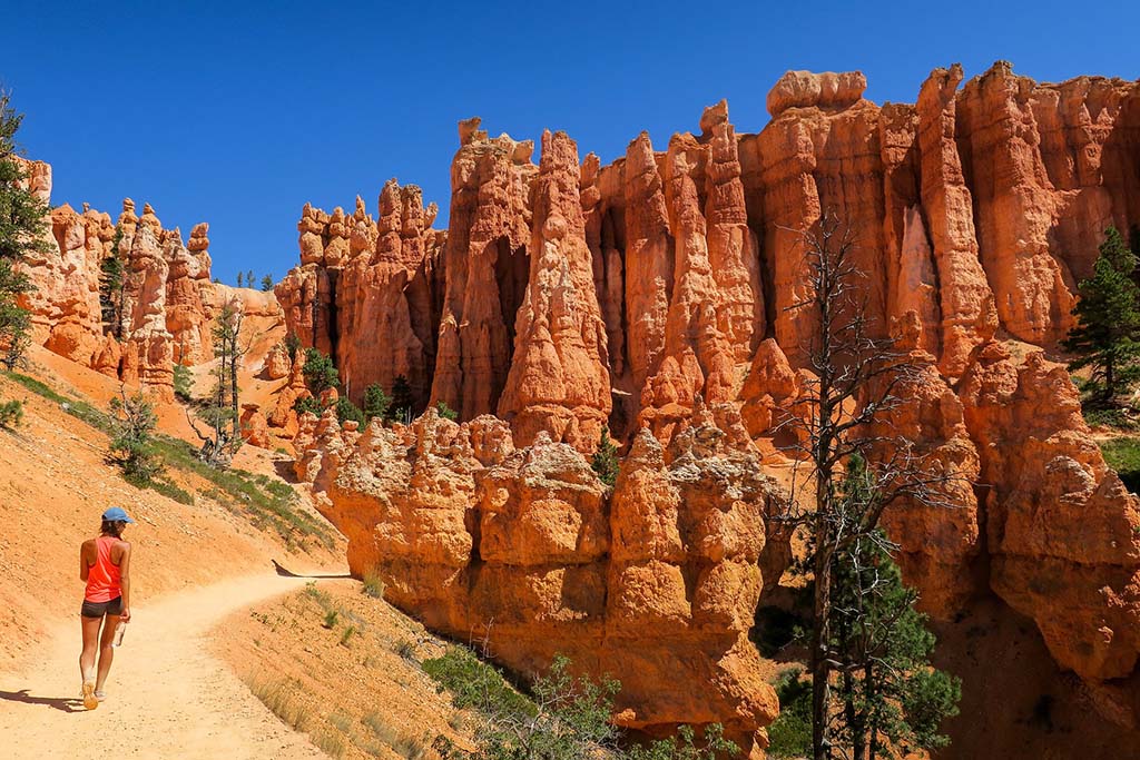 12 Beautiful Hikes in Bryce Canyon National Park 5 A woman enjoys Bryce Canyon hikes through orange hoodoos on a cloudless blue day