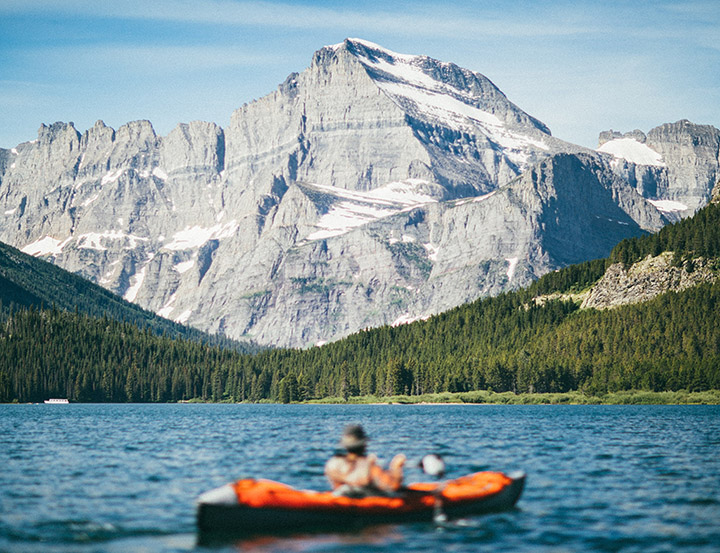 A man kayaking on a blue lake below a granite peak