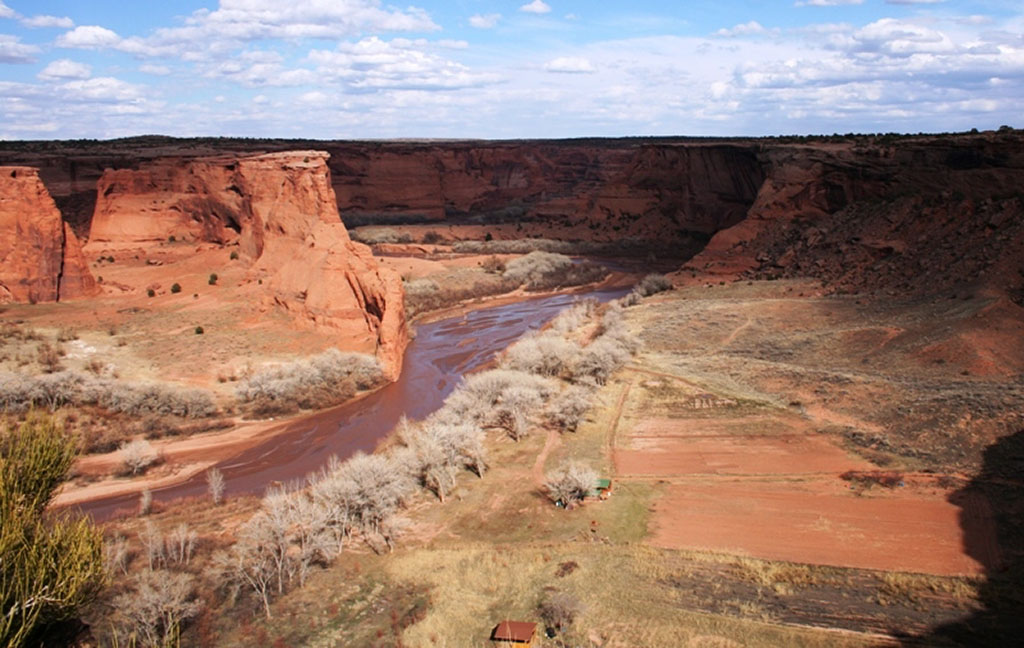 22 Amazing National Parks in Arizona 3 A shallow river runs through the bottom of a red canyon at one of the national parks in Arizona, Canyon de Chelly