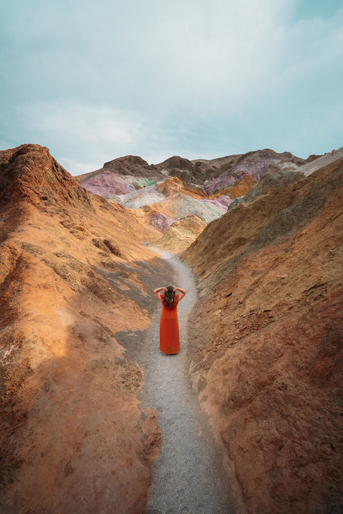 2 Day Death Valley Itinerary: How to See the Best of the West in 2 Days 3 A woman stands in a red dress on a trail surrounded by colored rock formations