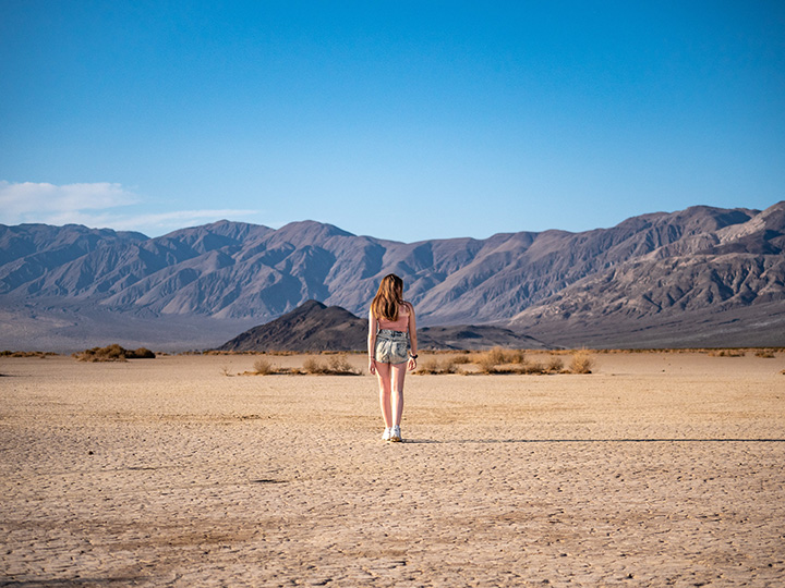 A woman stands alone on the sand with mountains in the background while spending two days in Death Valley itinerary