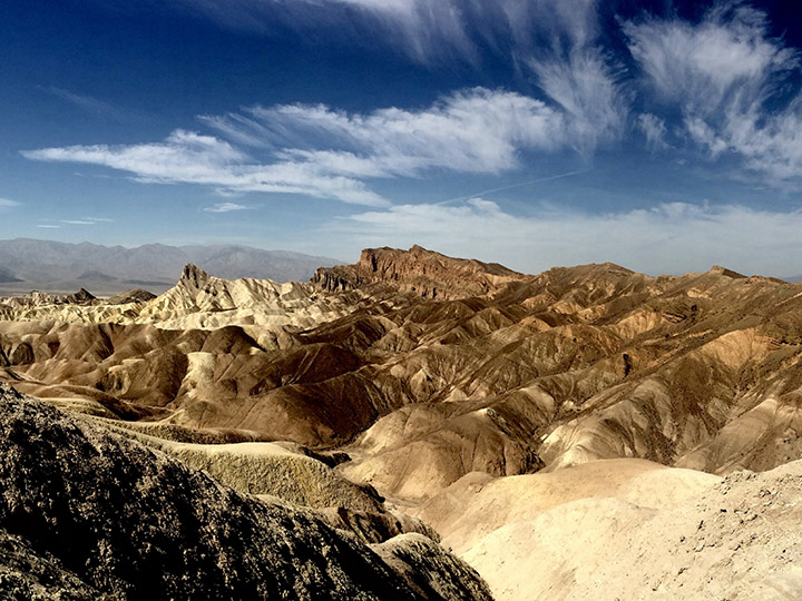2 Day Death Valley Itinerary: How to See the Best of the West in 2 Days 23 Colorful rock formations below a partly cloudy sky. Zabriskie Point is a must-see on a Death Valley itinerary