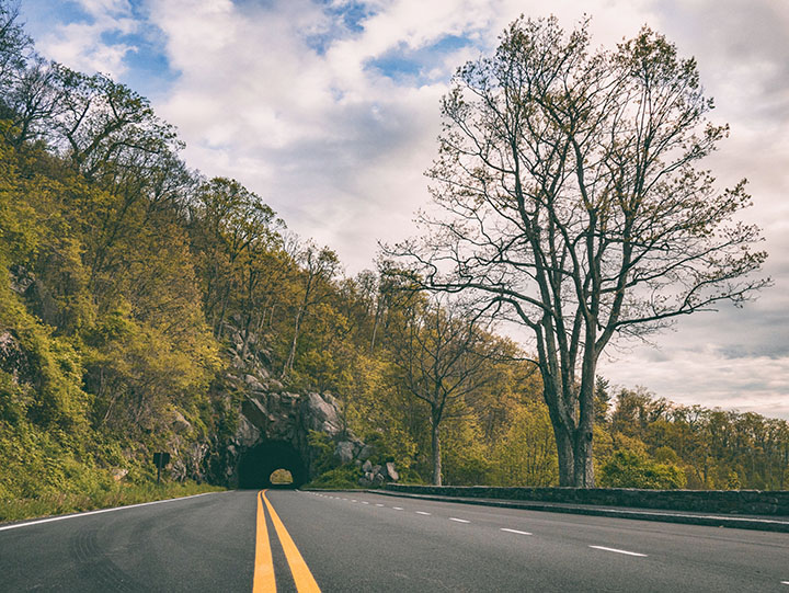 Shenandoah Camping: A Comprehensive Guide to All 5 Shenandoah Campgrounds 3 A paved road with solid yellow lines leads to a small tunnel through a mountain, seen while camping in Shenandoah