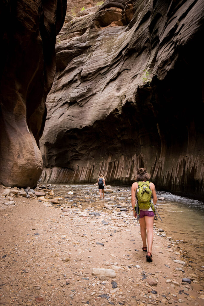 One Day in Zion: 4 Ways to Spend an Epic 24 Hours in Zion National Park 37 Two female hikers walking in and along a river in a canyon