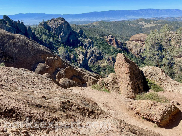 14 Phenomenal Things to Do in Pinnacles National Park 4 A trail meanders through red rock spires with mountain vistas in the background