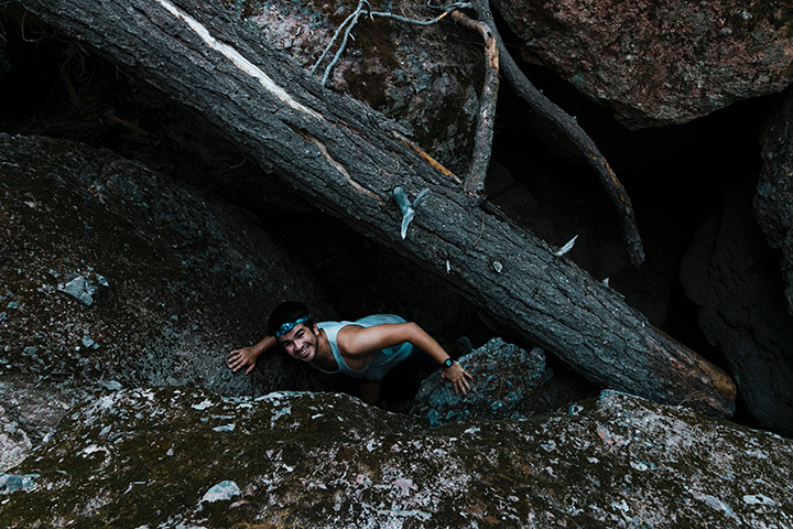 14 Phenomenal Things to Do in Pinnacles National Park 21 A man with a headlamp crawls through a cave under a tree. Exploring talus caves is one of the best things to do in Pinnacles National Park.