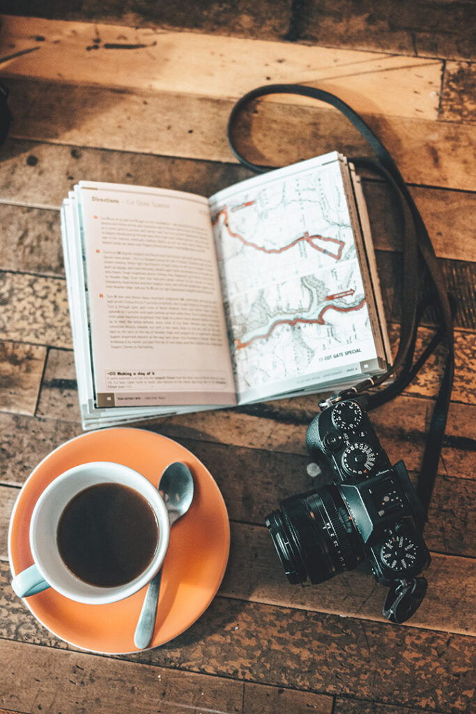 The 31 Best National Park Books for Every Reader 2 A book with a map is open on a table with coffee and a camera