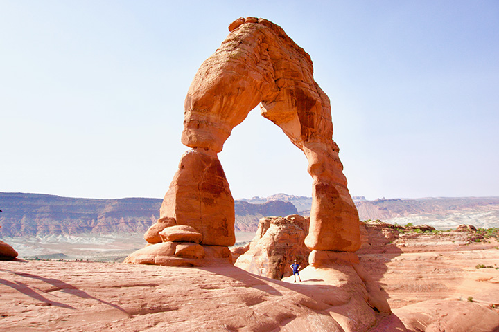 A hiker stands underneath Delicate Arch