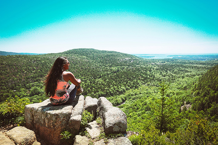 The Best Time to Visit Acadia National Park: When to See Fall Colors 12 A female hiker takes in the view from the top of a rock