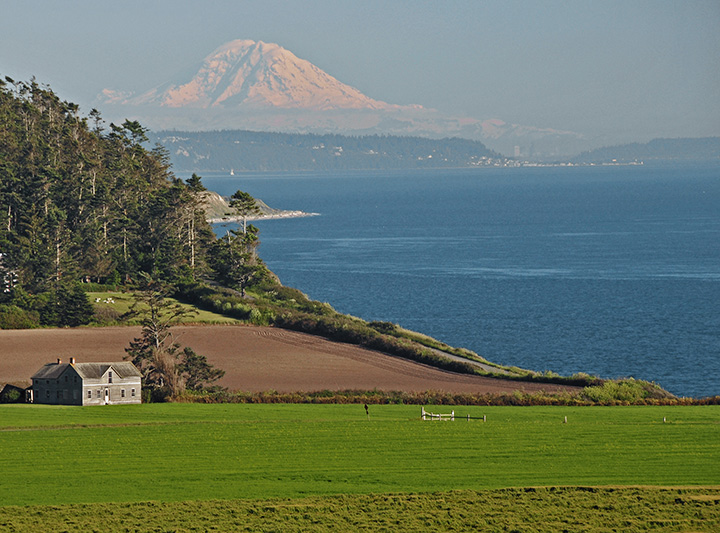 15 Wonderful National Parks in Washington 4 The Ferry House, an old wooden building, on the shore of Puget Sound with a snow-covered Mount Rainier in the background