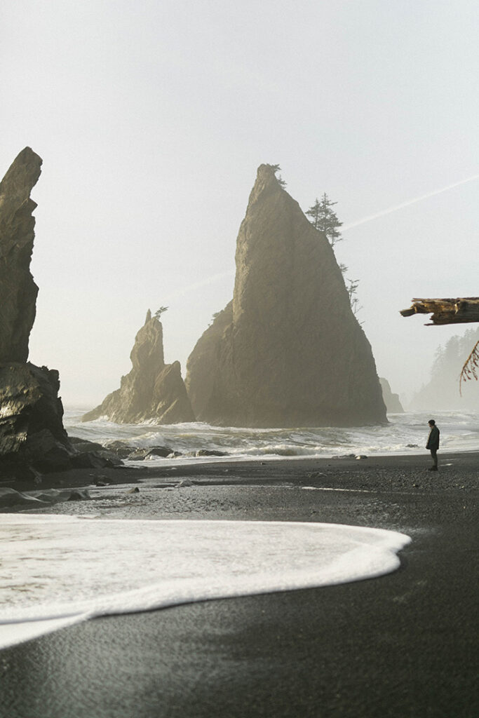 Olympic National Park Camping Guide: Everything You Need to Know About All 15 Olympic National Park Campgrounds 25 A hiker stands on a sandy beach near rock pinnacles standing in the ocean