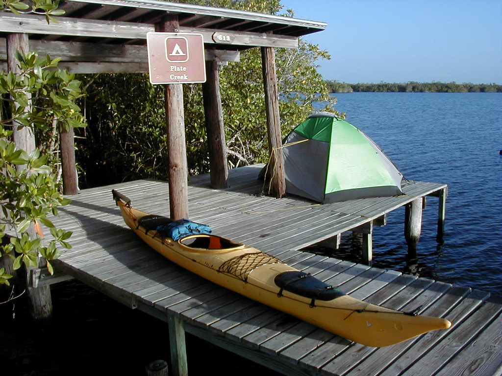 Everglades National Park 18 A wooden platform, known as a chickee, is used for camping in Everglades National Park. The platform sits above blue water. On the platform is a yellow kayak and a green tent tied to a wooden post.