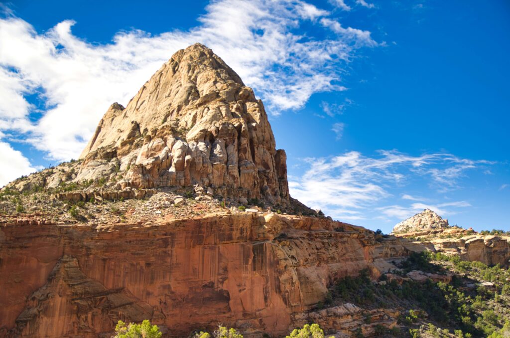 20 Best Hikes in Capitol Reef National Park 8 A yellow and orange rock formation below bright blue skies with wispy clouds