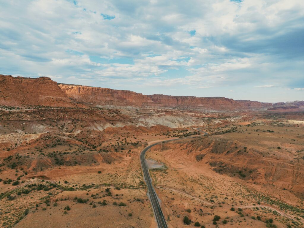 20 Best Hikes in Capitol Reef National Park 9 A paved road winds through scenic orange geologic formations on a partly cloudy day