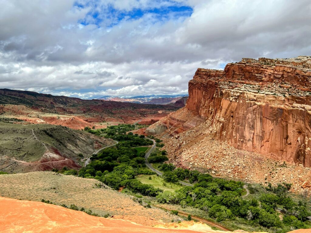 20 Best Hikes in Capitol Reef National Park 6 Green foliage lines the shores of a river in a valley below an orange canyon