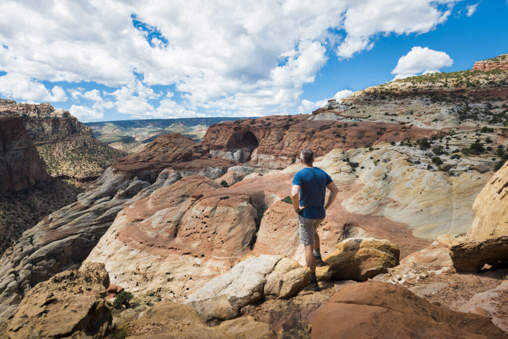 20 Best Hikes in Capitol Reef National Park 26 A hiker in a blue shirt peers out over the valley view from the top of Cassidy Arch, one of the best hikes in Capitol Reef National Park
