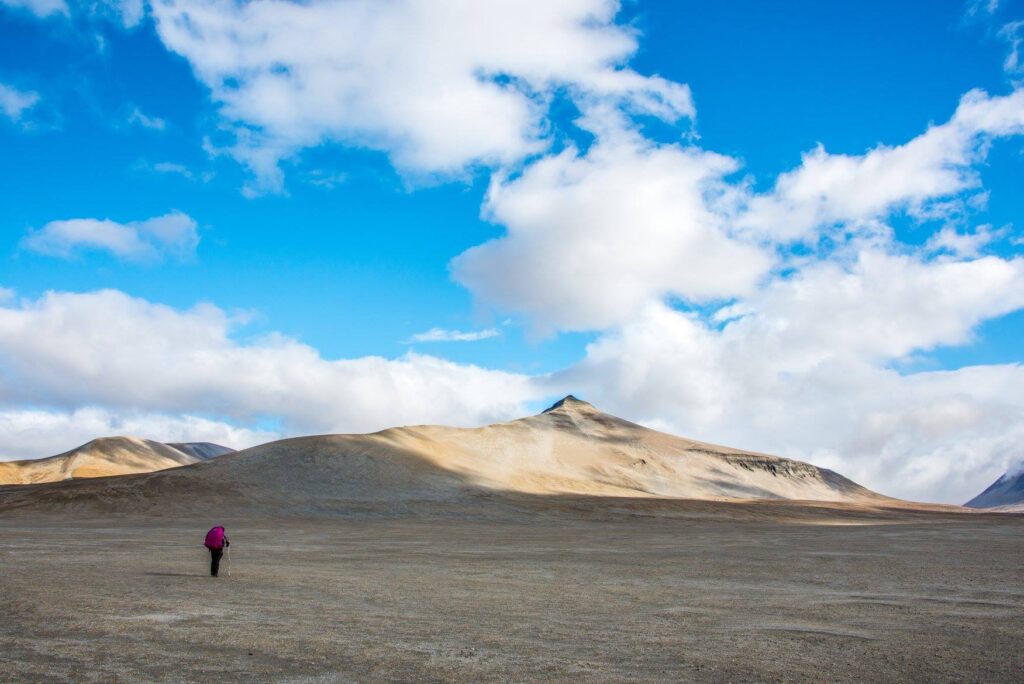 How to Get to Katmai National Park: Boats, Planes, and Bears, Oh My! 8 A lone hiker with a red backpack walks across an arid brown landscape under a blue sky