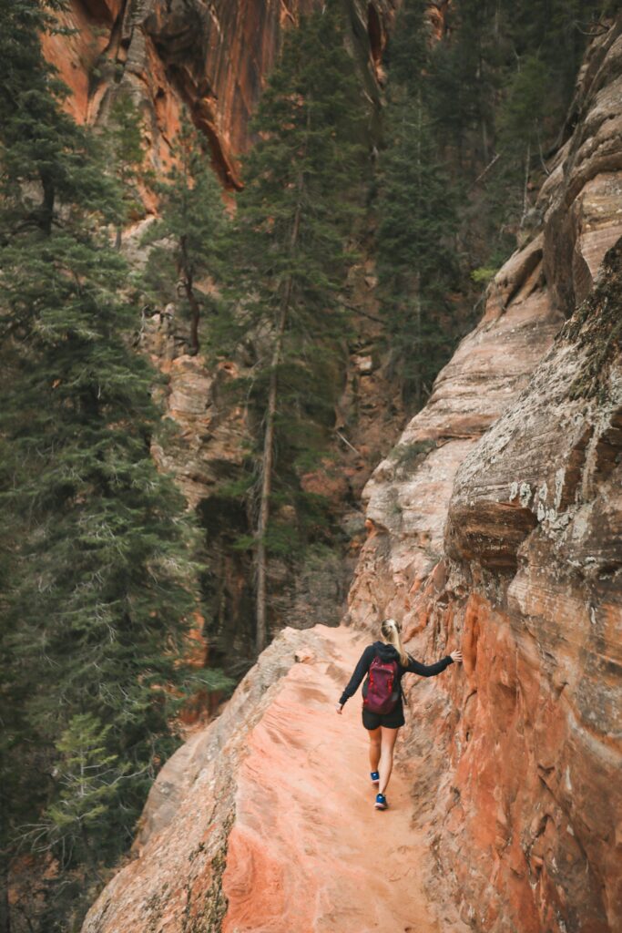 Closest Airports to Zion National Park: How to Get to Zion National Park, Utah 8 A hiker with arms outstretched walks along a mountain path